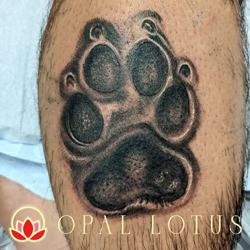 A memorial tattoo of a dog paw adorns a man's leg.