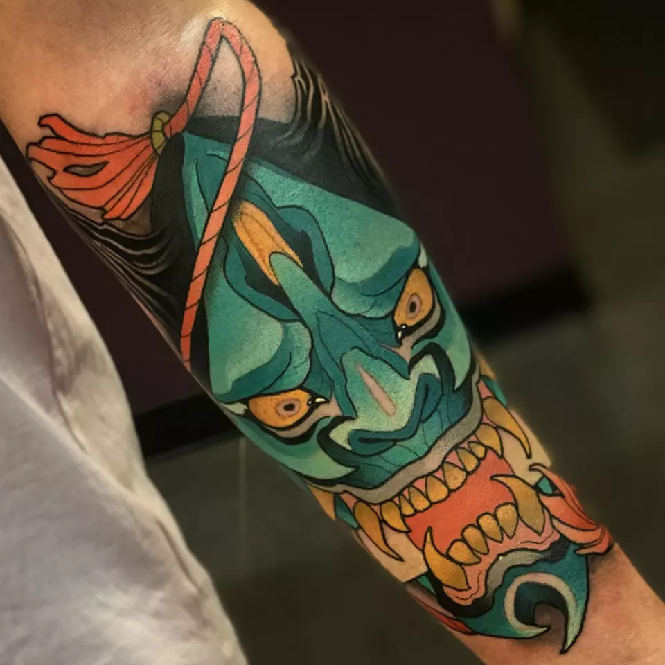 A forearm tattoo featuring a traditional Japanese mask, representing the rich culture and history of Japanese style tattoos.