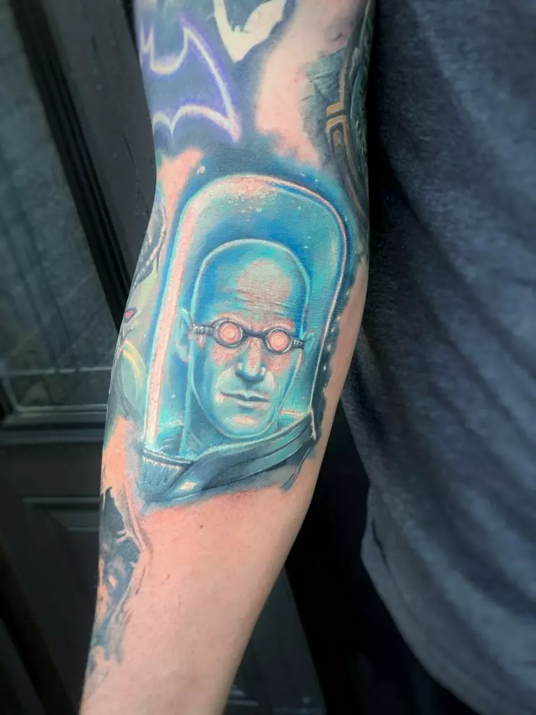 A realistic black work tattoo of a man with glasses on his arm.