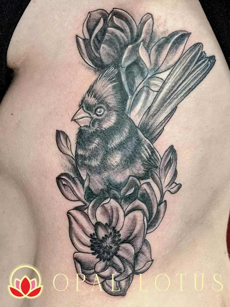 A tattoo featuring a bird and flowers in black and grey.
